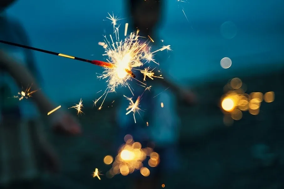 夜のビーチで鮮やかに火花を散らす手持ち花火の様子