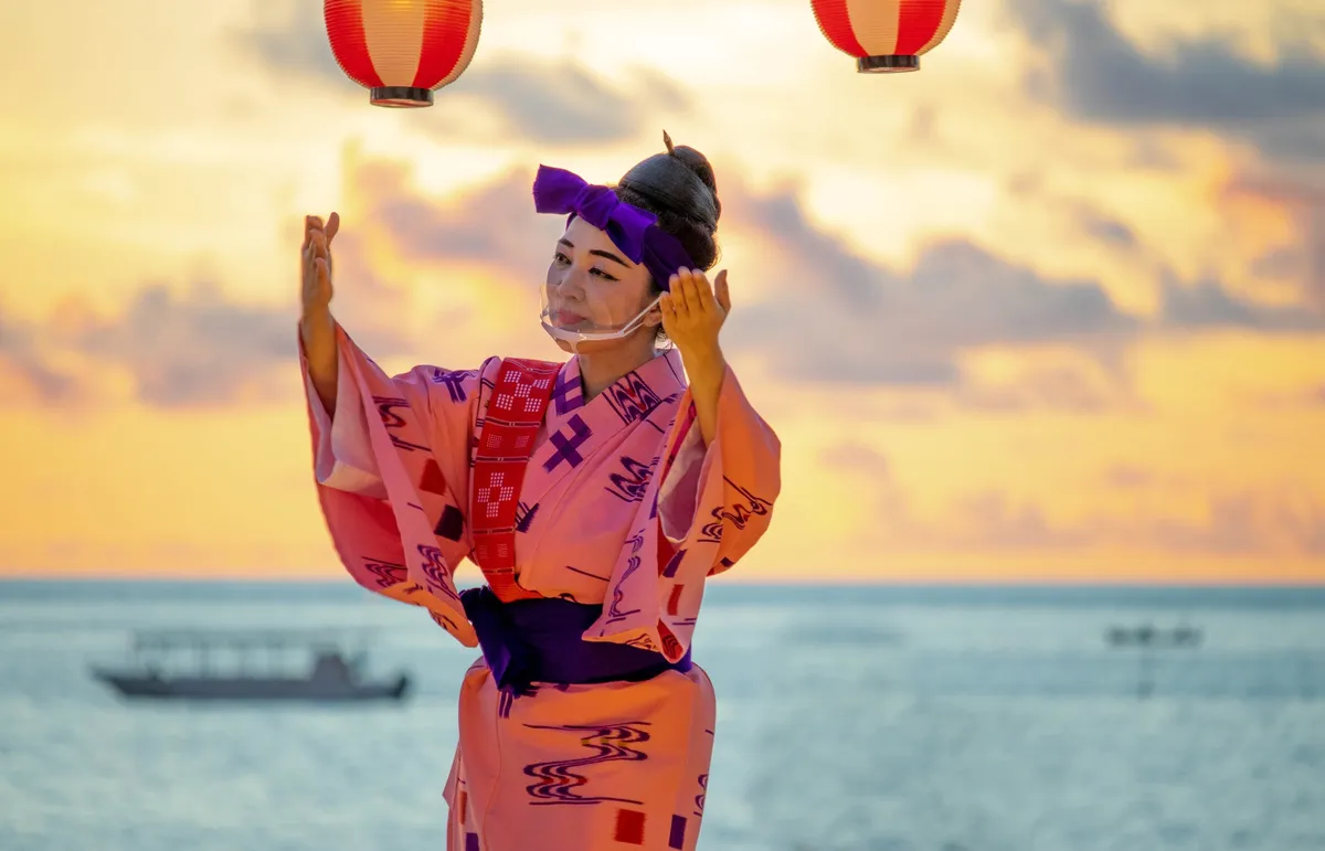 夕暮れのビーチを背景に沖縄の伝統衣装で踊る女性